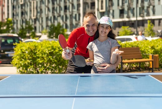 Family playing table tennis outside house.