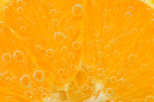 Slice of orange fruit in sparkling water. Orange fruit slice covered by bubbles in carbonated water. Orange fruit slice in water with bubbles. Close-up, macro horizontal image