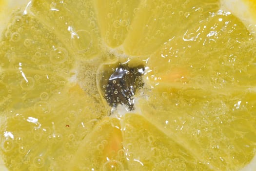 Close-up of a lemon slice in liquid with bubbles. Slice of ripe lemon in water. Close-up of fresh citron slice covered by bubbles. Macro horizontal image