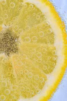 Slice of ripe lemon in water on white background. Close-up of lemon in liquid with bubbles. Slice of ripe citron in sparkling water. Macro image of fruit in carbonated water