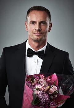 Portrait of mature man, suit and bouquet of flowers, handsome and isolated on grey background. Luxury, romance and rich celebrity actor fashion with romantic sexy date for valentines day and love