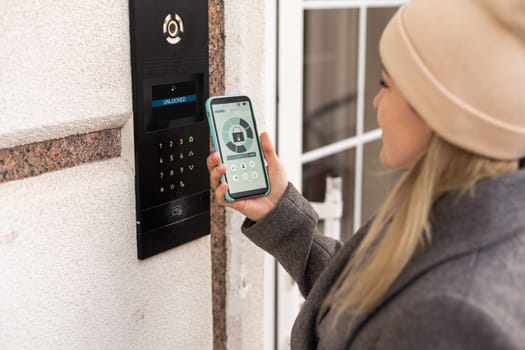 Woman locking smartlock on the entrance door using a smart phone. Concept of using smart electronic locks with keyless access