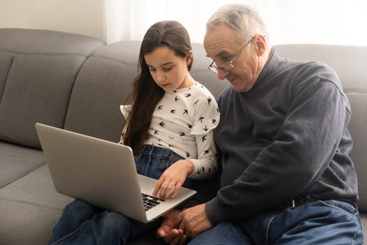 Happy retirement grandfather and pretty granddaughter laughing while watching e-book for learning to education together by laptop. Family educational at home concept. Technology and education