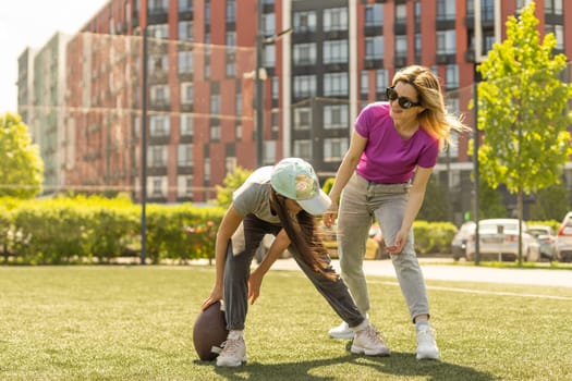 mother, daughter, oval brown leather rugby ball playing american football in park. Family and kids, nature concept