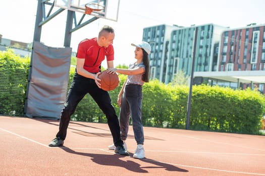 Happy father and teen daughter embracing and looking at camera outside at basketball court