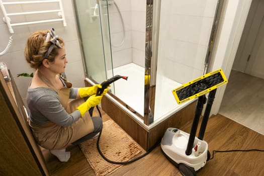 Woman doing bathroom cleaning at home, female washing tile wall with steam. Using steam cleaner for quick cleaning.