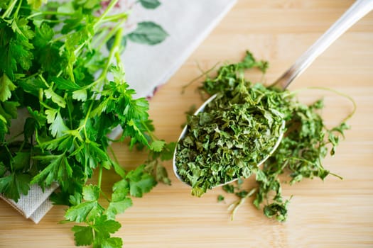 dried parsley in a spoon on a wooden table next to fresh herbs.