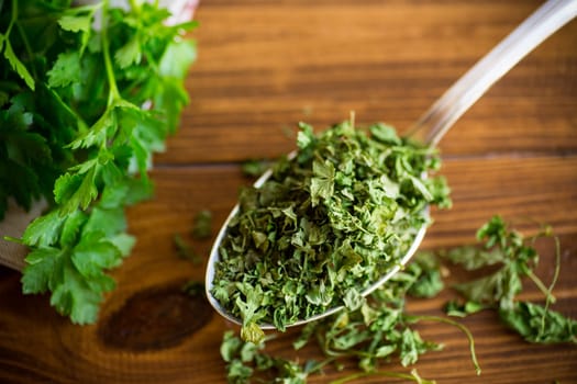 dried parsley in a spoon on a wooden table next to fresh herbs.