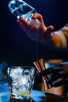 The bartender pours alcohol into a jigger. Bartender is preparing a cocktail at the bar. A smoky atmosphere in bar on the dark background. Selective focus