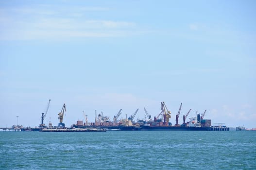 Many logistic transportation ships with cranes to move cargos around floating in the ocean on sunny day