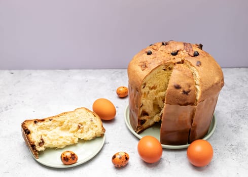 Cut Easter Panettone Italian Cake On Table With Colored Easter Hen, Quail Eggs. Fruitcake, Sweet Bread From Milan, Italy. Pastry Dessert. Pasqua Christian Cultural Holiday. Horizontal Plane