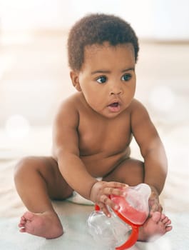 Kids, baby and black girl with a bottle sitting on a blanket on a home floor for child development. Children, cute and curious with a thirsty newborn infant learning or growing alone in a house.