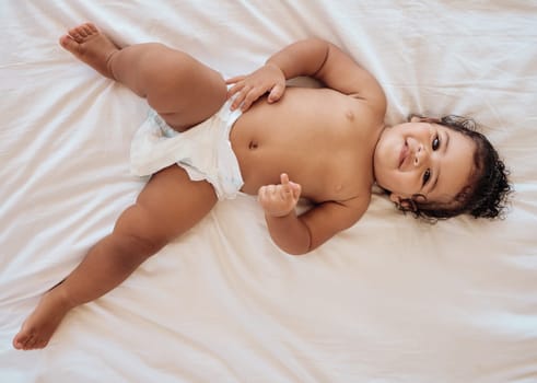 Happy baby, smile and relax on bed in family home bedroom for diaper change, bedtime or healthy childcare. Child, happiness and body care in disposable nappy or kids portrait from above in nursery.