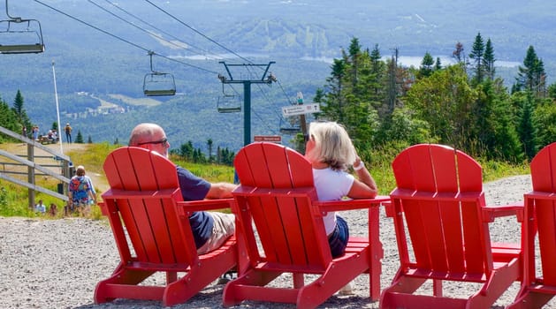 Sightseeing mountain views at Mont Tremblant ski Resort in summer. Tourists enjoying sitting at red chairs at ski resort village. Mont-Tremblant, Quebec, Canada - 22.09.2022.