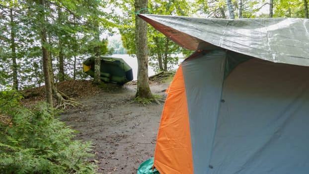 Camping and tent under the pine forest near the lake with beautiful sunlight in the morning. Green boat near the lake