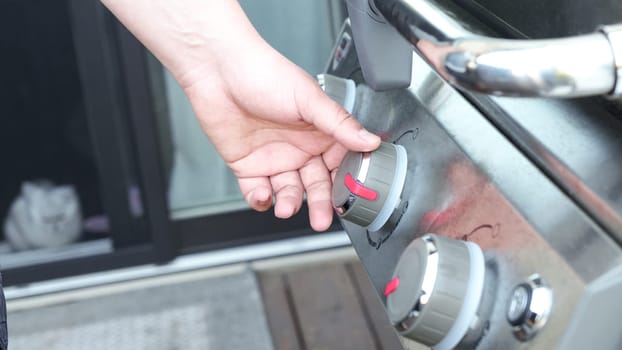 Hand is holding Grill knob gas to heat the bbq. Power heat temperature, starter lighter chrome cook appliance on off.