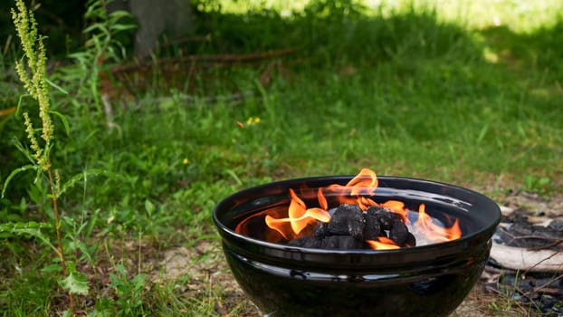 Black round Barbecue Grill with Fire on Open Air with green grass. Fire Flame. Prepairing charcoal for the grilling bbq outdoors