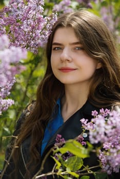 Portrait of a beautiful young woman surrounded by lilac flowers.