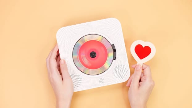 Hands holding white cd player with red disc and heart shape gift card on yellow background. Love music, Valentine day, Greeting, retro Love song, space for text