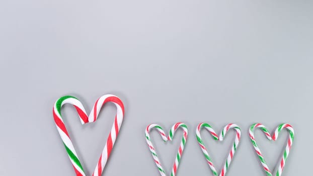 Red, green and white candy canes in the shape of heart on grey background. Valentine's Day concept. Greeting card with copy space for your text or advertising, flat lay