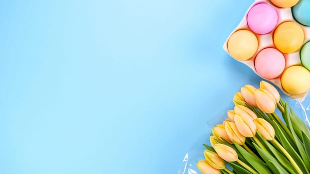 Spring flat lay with fresh yellow tulips colorful eggs on blue background. Easter, Mother day, birthday or Anniversary with copy-space. Sweet rainbow color Easter eggs, small pastel colors