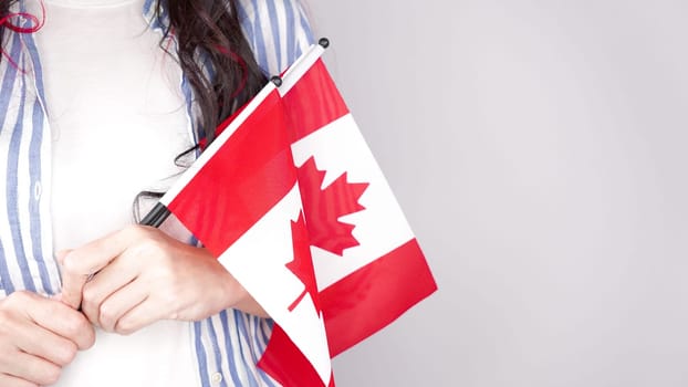 Unrecognized girl student in white blue shirt holding small canadian flag over gray background, Canada day, holiday, vote, immigration, tax, copy space.