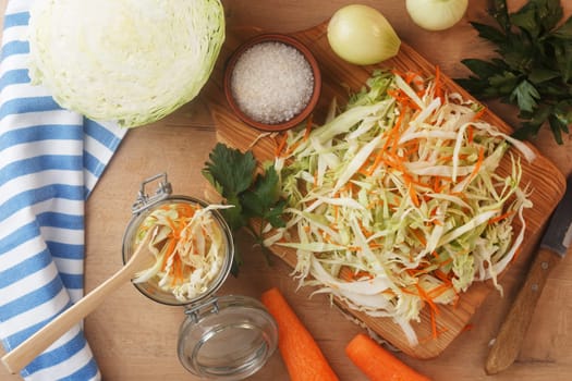 Sliced cabbage on a wooden board with carrots, onions and herbs. Preparing to cook coleslaw