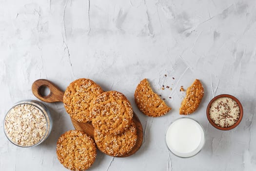 Oatmeal cookies with sesame seeds and flax seeds on a gray background with a jar of oatmeal and a glass of milk.Copy space