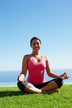 Yoga centres her. A gorgeous young woman in a yoga position smiling while sitting on the grass