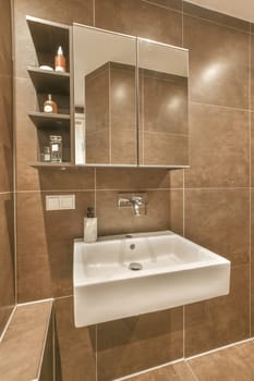 a bathroom with brown tiles and white fixtures on the wall, including a mirror over the sink basin in the corner