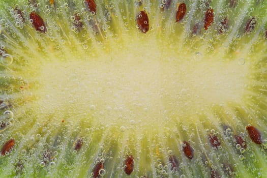 Close-up of a kiwi fruit slice in liquid with bubbles. Slice of ripe kiwi fruit in water. Close-up of fresh kiwi slice covered by bubbles. Macro horizontal image