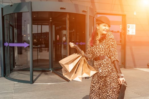 A happy shopaholic girl keeps her bags near the shopping center. A woman near the store is happy with her purchases, holding bags. Dressed in a leopard print dress. Consumer concept