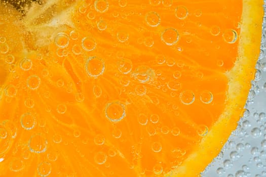 Close-up of an orange fruit slice in liquid with bubbles. Slice of ripe orange fruit in water. Close-up of fresh orange fruit slice covered by bubbles. Macro horizontal image