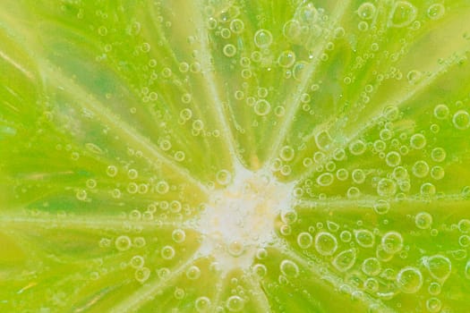 Close-up of a lime slice in liquid with bubbles. Slice of ripe lime in water. Close-up of fresh lime slice covered by bubbles. Macro horizontal image