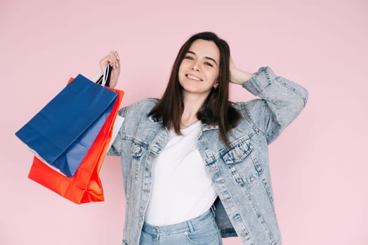 Joyful Shopper: Young Woman in Denim Shirt Celebrating, Arm Raised in Excitement, Against Pink Background, Delighted by Online Shopping or Amazing Find.
