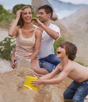 Family, laughing and sand castle at beach in summer for fun, travel or holiday with love. A man, woman and excited kid playing together on vacation at sea with a toy bucket, development and happiness.