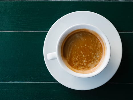 A cup of black coffee with foam on a emerald wooden background, top view. Espresso or americano. Cafe and bar, barista art concept. Minimalism