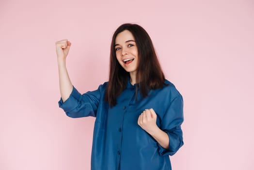 Triumphant Celebration: Photo of an Ecstatic Lady Raising Fists in Joyful Achievement, Embracing Success in an Empty Space, Isolated on a Vibrant Pink Background.
