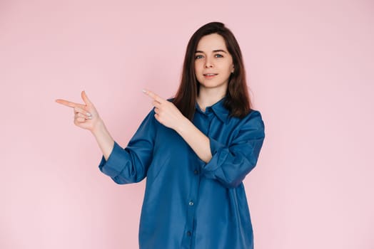 Cheerful Woman Pointing with Fingers at Empty Space, Conveying Information: Vibrant Photo on Pink Background.