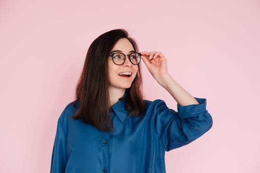 Smiling woman touching glasses, pondering and looking for ideas in empty space: Isolated portrait on pink background.