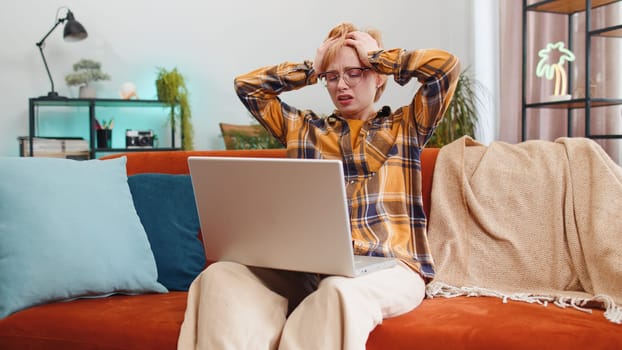 Displeased woman use laptop notebook typing browsing working, loses becoming surprised sudden lottery results bad news fortune loss fail computer virus. Portrait of girl at home in room on couch