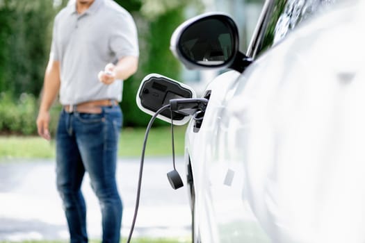 Focus recharging electric vehicle outdoor from charging station with blurred background of man at EV car. Concept ideal for new progressive technology of green and renewable energy for car.