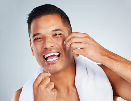 Man, dental flossing and teeth with smile for clean hygiene and health against a grey studio background. Portrait of happy toothy male smiling in fresh grooming and floss for mouth, oral and gum care.