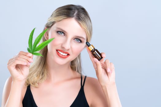 Alluring portrait of beautiful woman with perfect makeup hold green leaf, marijuan extracted bottle for skincare treatment product. Cannabis CBD oil for cosmetic and beauty in isolated background.