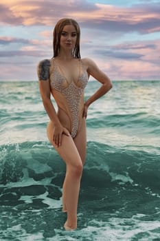 Portrait of a sensual looking attractive young woman with beautiful makeup and long hair posing on the beach in a beige swimsuit.