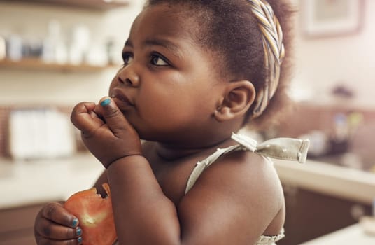 Black child, tomato and eating baby in a home kitchen with food and fruit at breakfast. African girl, nutrition and youth in a house with hungry kid feeling relax with natural, healthy snack for kids.