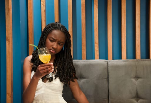 copyspace of afro girl on a gray sofa looking with a look between puzzled and dislike or disgust at her cocktail. High quality photo