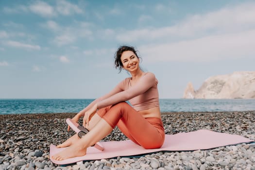 Middle aged well looking woman with black hair doing Pilates with the ring on the yoga mat near the sea on the pebble beach. Female fitness yoga concept. Healthy lifestyle, harmony and meditation.