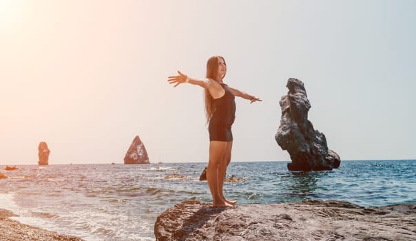 Woman travel sea. Young Happy woman in a long red dress posing on a beach near the sea on background of volcanic rocks, like in Iceland, sharing travel adventure journey