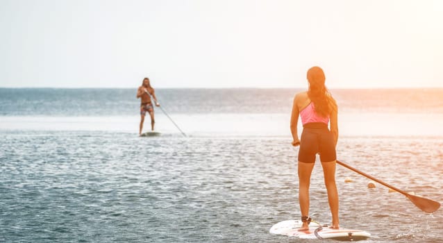 Sea woman and man on sup. Silhouette of happy young woman and man, surfing on SUP board, confident paddling through water surface. Idyllic sunset. Active lifestyle at sea or river